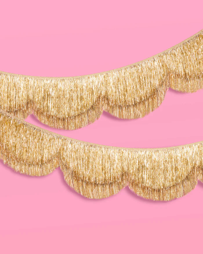 Two gold scalloped fringe banners layered on pink background, close-up detail shot