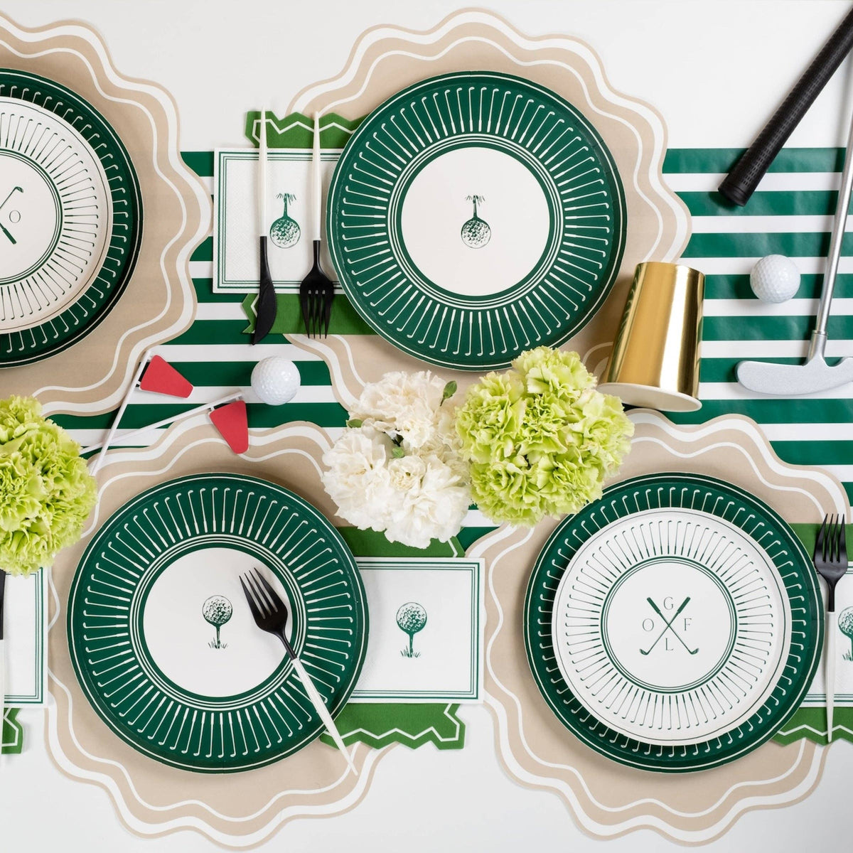 An overhead flat lay of a complete golf-themed tablescape with golf party plates, "Hole in One" pennants, gold cups, and a green striped table runner for a Masters watch party.
