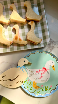 A full view of a snack table with goose shaped sandwiches and napkins, with a goose themed paper plate.