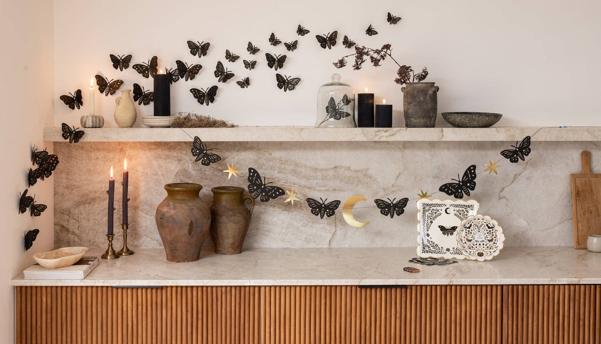 Wide room shot of the full gothic Halloween scene — black moth wall swarm across a marble shelf with moth napkins, candles, and dark-academia styling below.