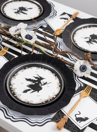 Overhead view of a gothic Halloween place setting featuring the witch plate, a striped paper runner, white florals, and gold flatware.