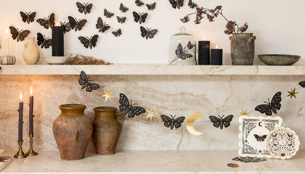 Wide gothic Halloween marble shelf scene with moth wall swarm, crescent moon, Moonlight plate and napkin, dark pottery, and lit candles.