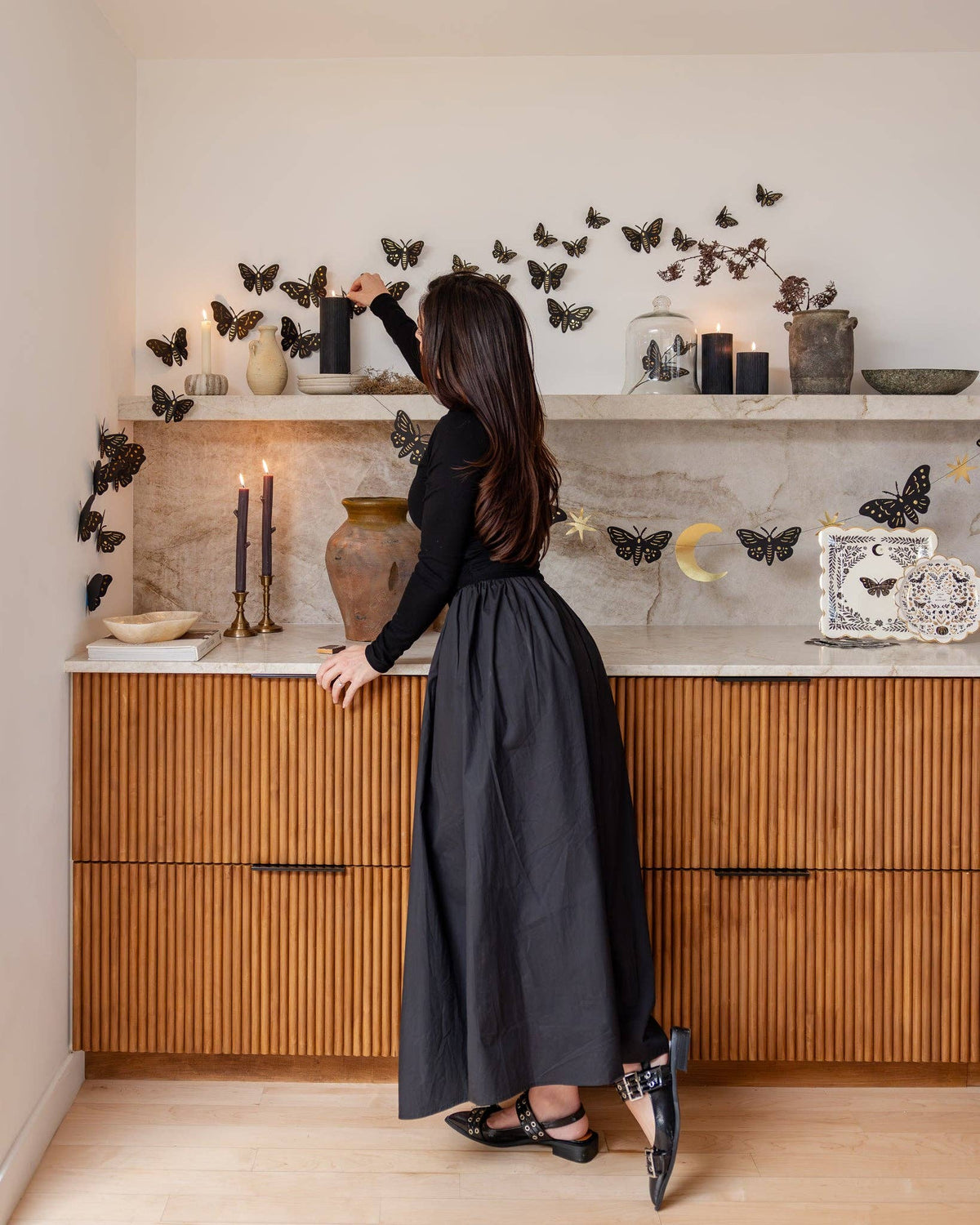Wide room shot of the full moth wall swarm above a wood-paneled counter with marble top, candles lit, pottery — dark-academia gothic Halloween room.