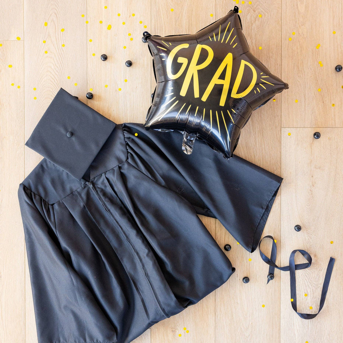 Black graduation gown with grad star mylar balloon and confetti flat lay
