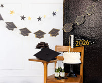 Graduation party table setup with black and gold banners, pennant, cake, and decorations