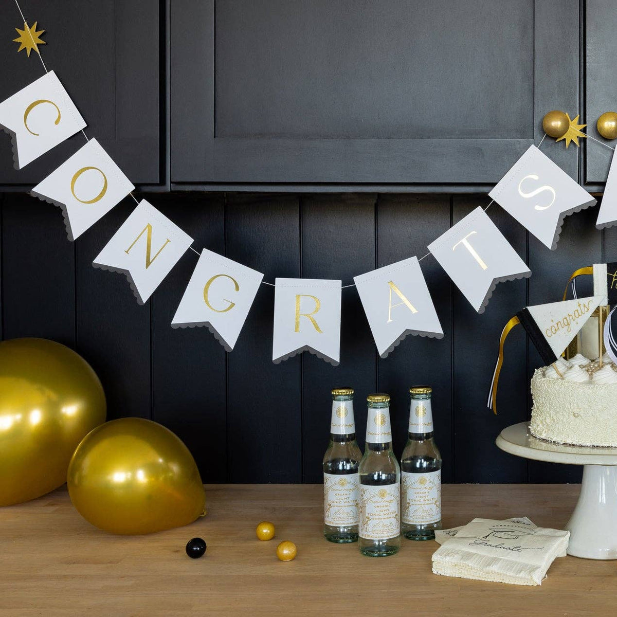 Graduation party setup with Congrats Grad banner, gold balloons, and cake table
