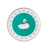 Green Christmas dessert plate with a white swan wearing a red bow in the center and a cream rim of green sprigs and holly, gold-trimmed edge, overhead view on white background.