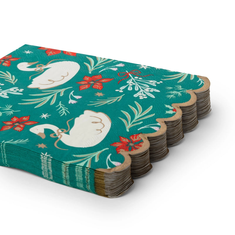 Stack of folded green swan Christmas paper napkins showing the floral print and gold scalloped edge from an angle.
