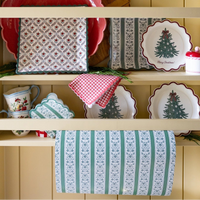 Green floral stripe paper table runner draped from a cream kitchen hutch below Christmas tree plates, red gingham napkins, and square floral plates