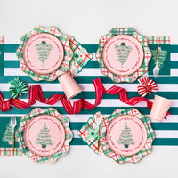 Holiday tablescape with pink salad plates on top of scalloped green plaid plates styled with ribbon and cups—coordinated Christmas party decorations.