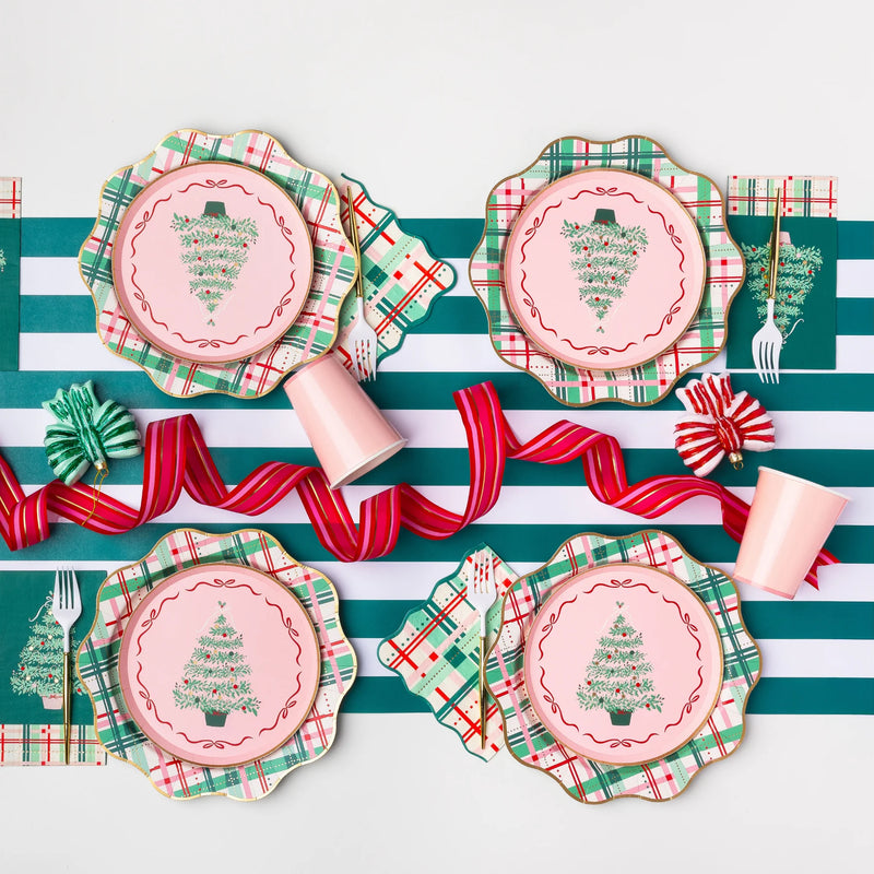 Holiday tablescape with pink salad plates on top of scalloped green plaid plates styled with ribbon and cups—coordinated Christmas party decorations.