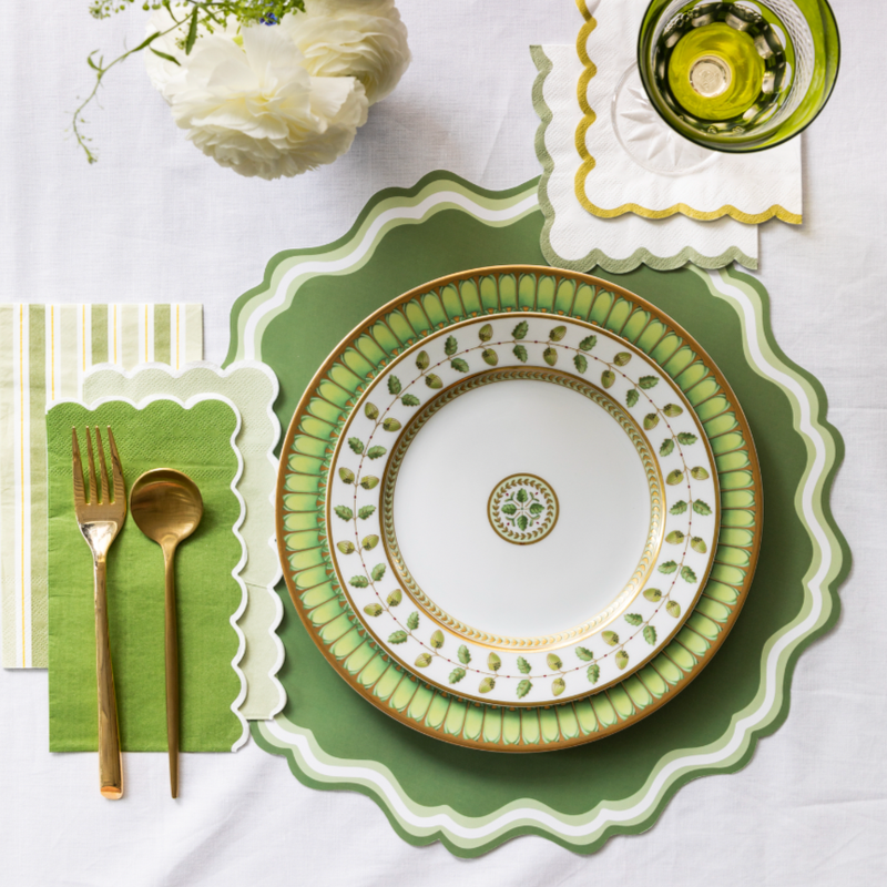 Green place setting with the scalloped placemat under a gold-rimmed green-and-white plate, gold flatware, and a green striped napkin.