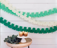 Green and cream shamrock paper garlands hanging on a white wood wall
