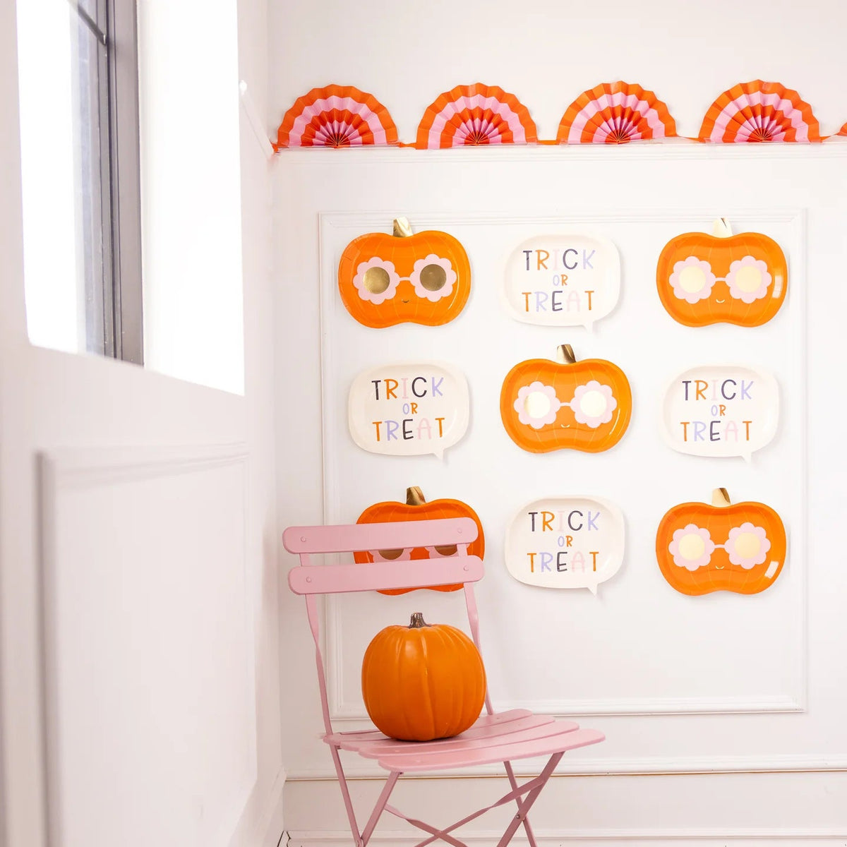 Wall gallery of alternating pumpkin and word-bubble plates above a pink chair with real pumpkin—shows decorative versatility beyond dining.