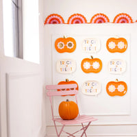 Wall gallery of alternating pumpkin and word-bubble plates above a pink chair with real pumpkin—shows decorative versatility beyond dining.