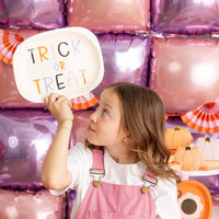 Girl gazes at word-bubble plate she’s raising, surrounded by matching groovy pumpkin tableware—conveys plate’s playful, kid-approved vibe.