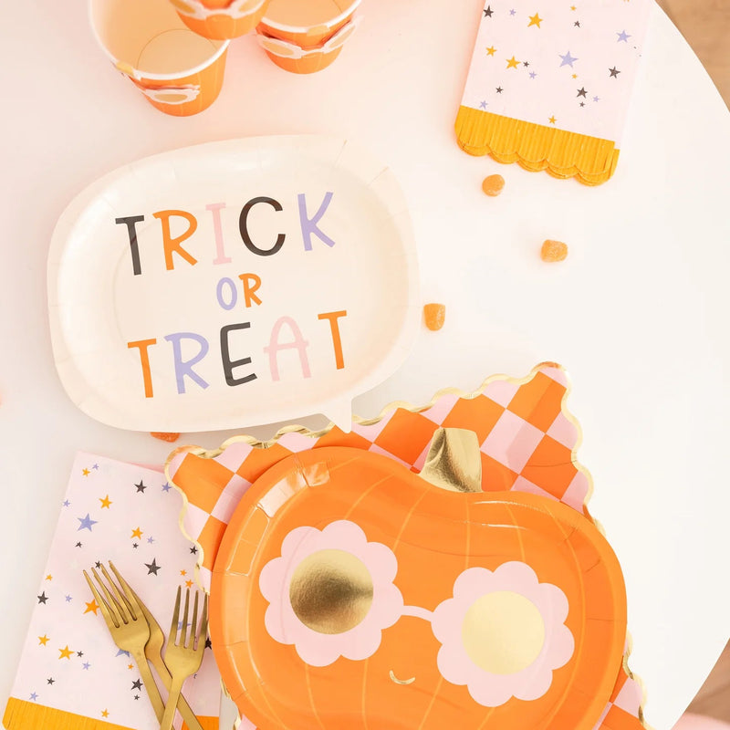 Styled overhead table with speech-bubble plate, pumpkin plate, star napkin, gold forks, and candy—coordinated groovy Halloween party setup.