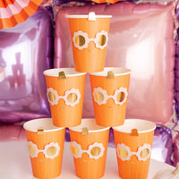 Stack of orange paper cups with white flower designs on a white surface.