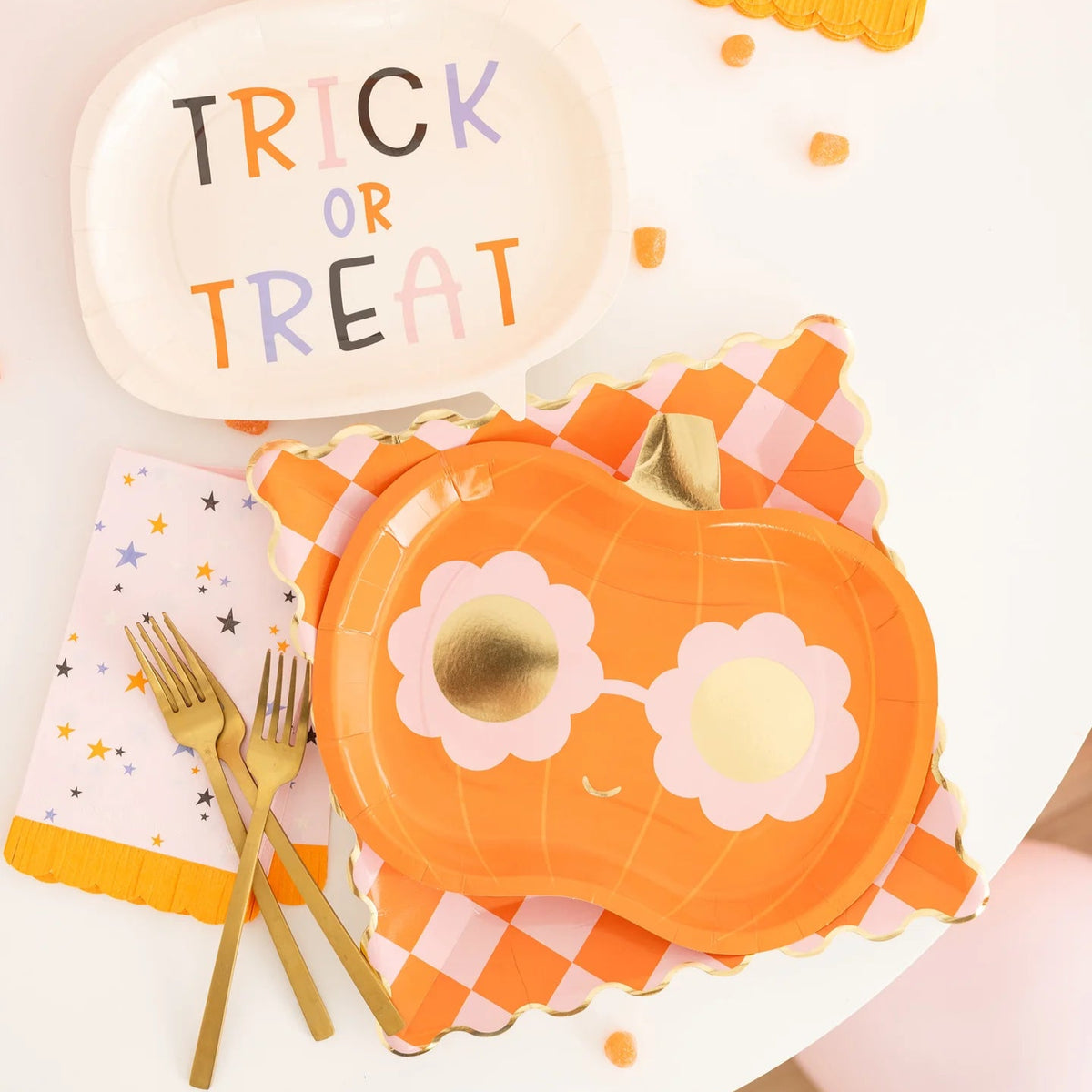 Pastel star napkin styled with pumpkin sunglasses plate, gingham charger and “Trick or Treat” speech-bubble dish on bright dessert table.
