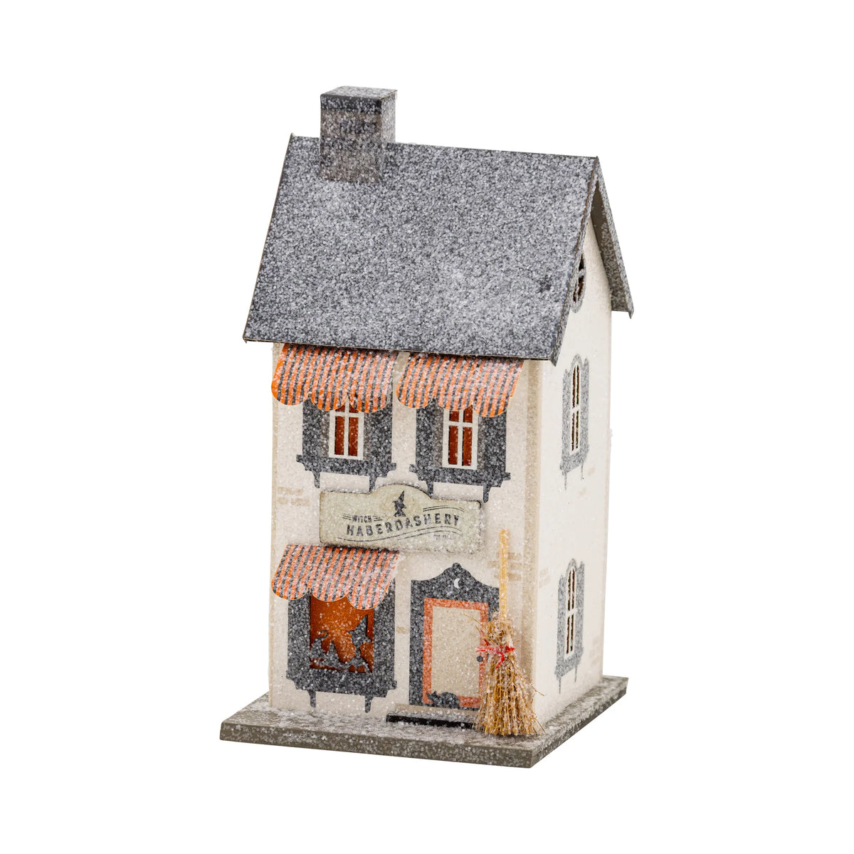 Front view of the Haberdashery haunted village house with orange awnings and lit windows, vintage putz-style Halloween décor.
