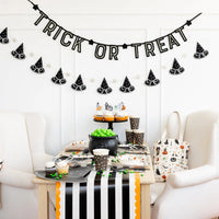 Black felt ‘TRICK OR TREAT’ halloween banner hanging above a witchy cupcake table with striped runner