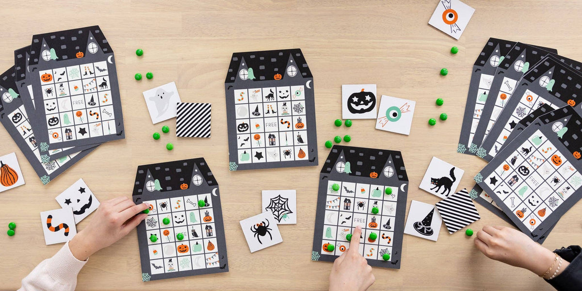 Halloween bingo game with three haunted house bingo sheets, calling cards and green candy markers on a wood table