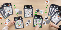 Halloween bingo game with three haunted house bingo sheets, calling cards and green candy markers on a wood table