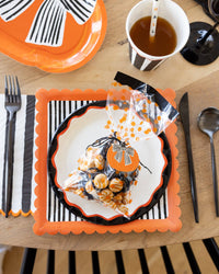 Halloween-themed table setting with decorative plates, cutlery, and a filled treat bag tied with a pumpkin tag and baker's twine, showing the clear cello and polka dots.