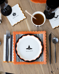 Halloween cocktail paper napkins styled on a Halloween tablescape with striped paper plate, orange placemat, black cups, and spooky party décor.