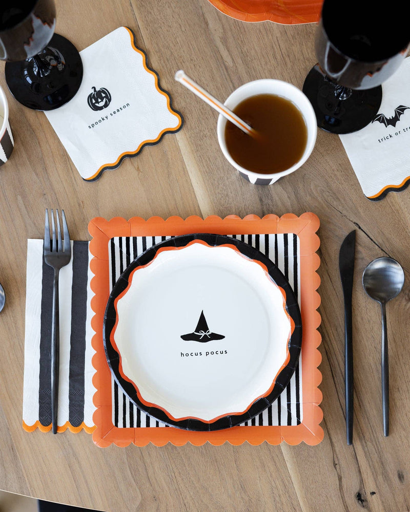 Halloween cocktail paper napkins styled on a Halloween tablescape with striped paper plate, orange placemat, black cups, and spooky party décor.