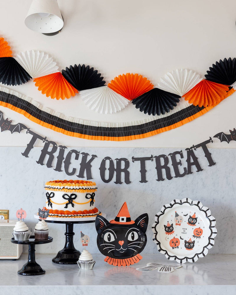 Halloween crepe garland strung above a marble counter with a black cat plate, vintage Halloween plates and an orange bow cake