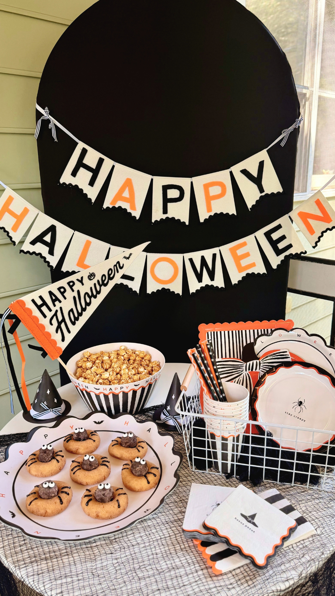 Black star-print and orange paper straws in a stack of Halloween party cups, displayed on a black and orange Halloween dessert table