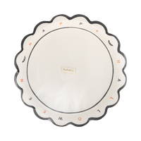 Angled overhead view of the cream Halloween dinner plate showing the spaced black and orange rim lettering, bat details, and My Mind's Eye logo in the center.
