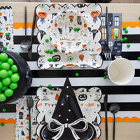 Halloween-themed table setting with decorative plates, cups, and utensils on a black and white striped tablecloth.
