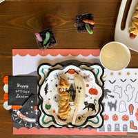 Overhead Halloween place setting with a scalloped icon placemat, a spiderweb taco dip on an icon plate, a chalkboard sign, and a cream cup