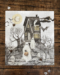 A completed jigsaw puzzle featuring a spooky Halloween scene with a haunted house, ghosts, bats, tombstones, and a full moon, displayed on a rustic dark wood background with a few loose puzzle pieces around it.