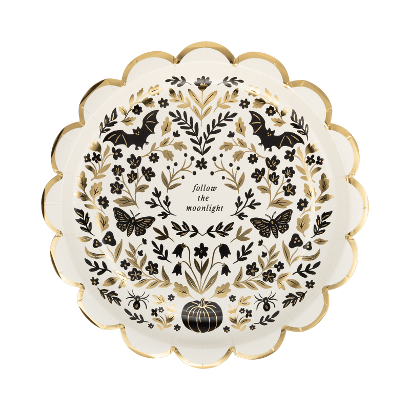 Cream Halloween dessert plate covered in a dense black folk-art pattern of moths, florals, crescent moons, pumpkins, and "follow the moonlight" text, with a gold foil scalloped edge, overhead view.