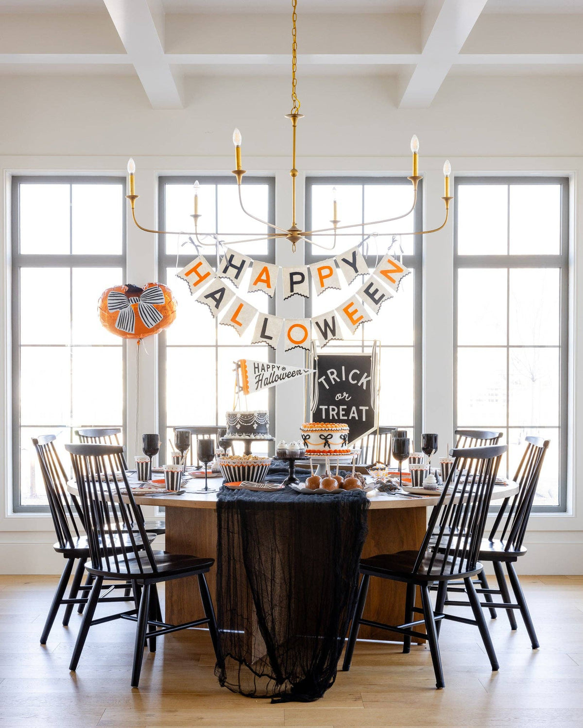 Wide styled Halloween party dining room with the pumpkin balloon, banner, black table, and spooky centerpieces.