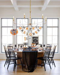 Wide styled Halloween party dining room with the pumpkin balloon, banner, black table, and spooky centerpieces.