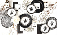 Flat lay of scattered black lace border plates, vintage witch dessert plates, and decorative spider webs on a white surface.