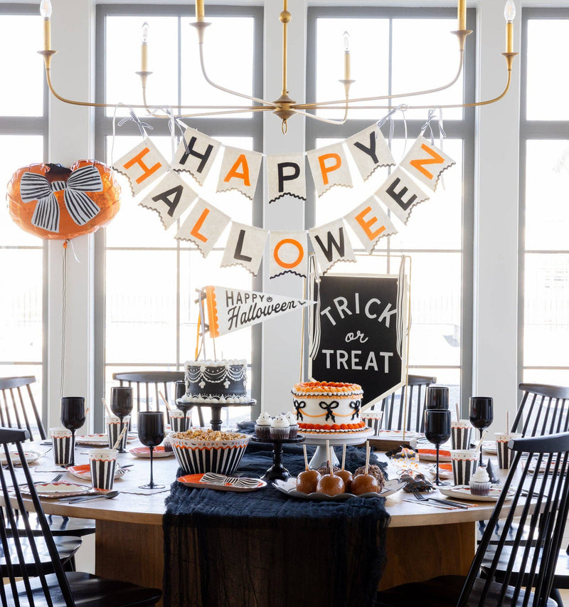 Styled Halloween party — the pumpkin balloon over a table with the "HAPPY HALLOWEEN" banner and "trick or treat" décor in a bright dining room.