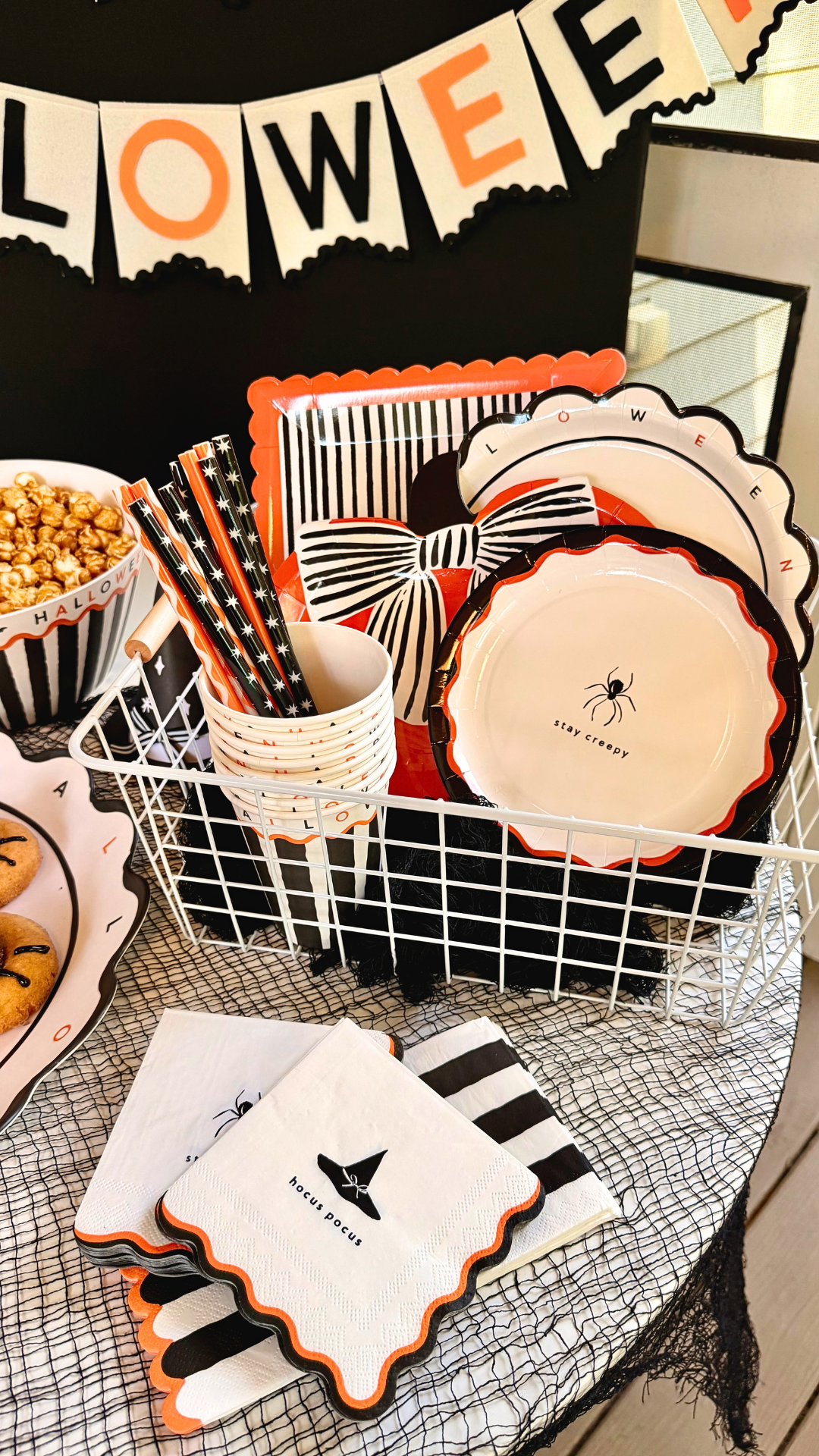 Hocus pocus witch hat and stay creepy spider Halloween napkins with scalloped orange and black edges, in front of a basket of party plates and cups