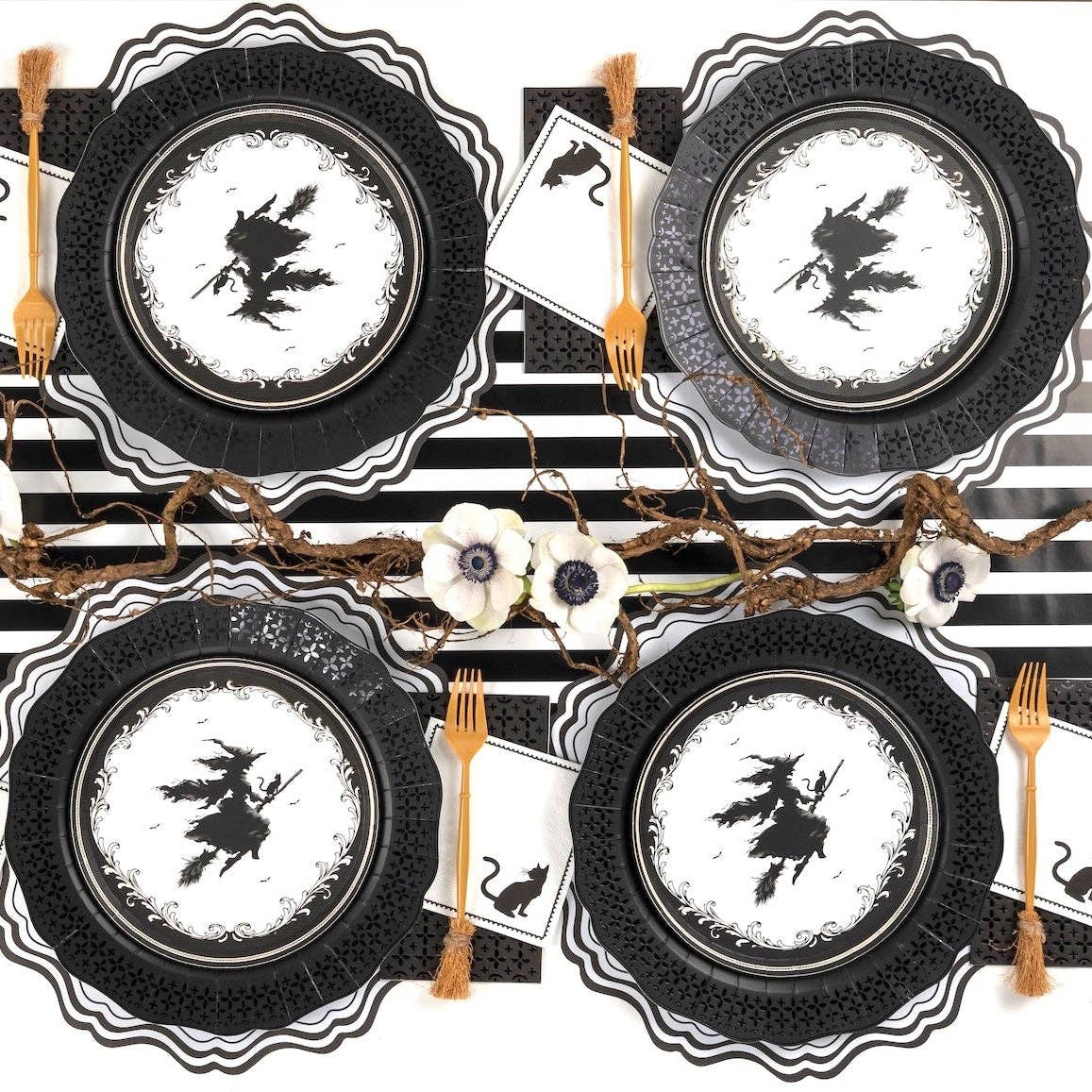 Halloween place setting with the black guest towel under a witch plate, gold flatware, on a black-and-white striped surface.