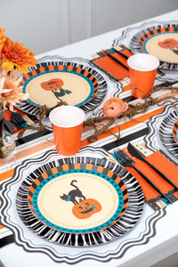 Halloween place setting detail showing the cat-and-pumpkin plate layered with the retro striped towel and orange accents.