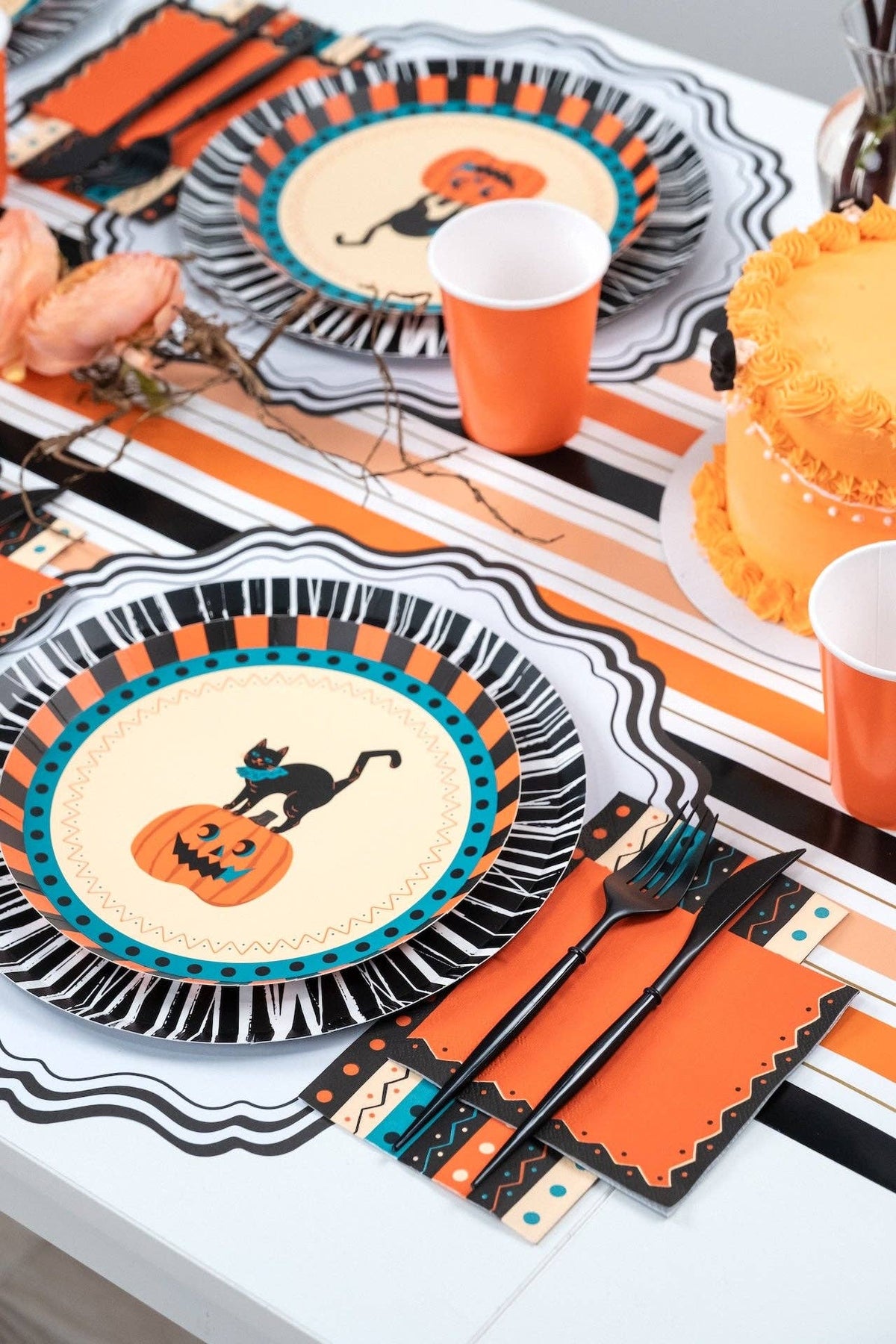 Vertical Halloween place setting showing the vintage cat-and-pumpkin fringe plate with the orange napkin and black flatware.