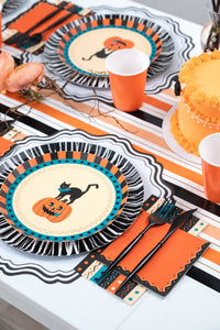 Vertical Halloween place setting showing the vintage cat-and-pumpkin fringe plate with the orange napkin and black flatware.