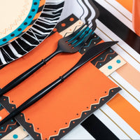 Halloween place setting close-up showing the orange napkin, black fringe plate, vintage cat-and-pumpkin illustration, and black flatware.