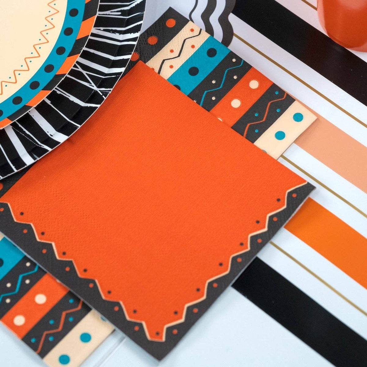 Halloween place setting close-up showing the retro striped guest towel folded beside the vintage cat plate with an orange scalloped napkin.