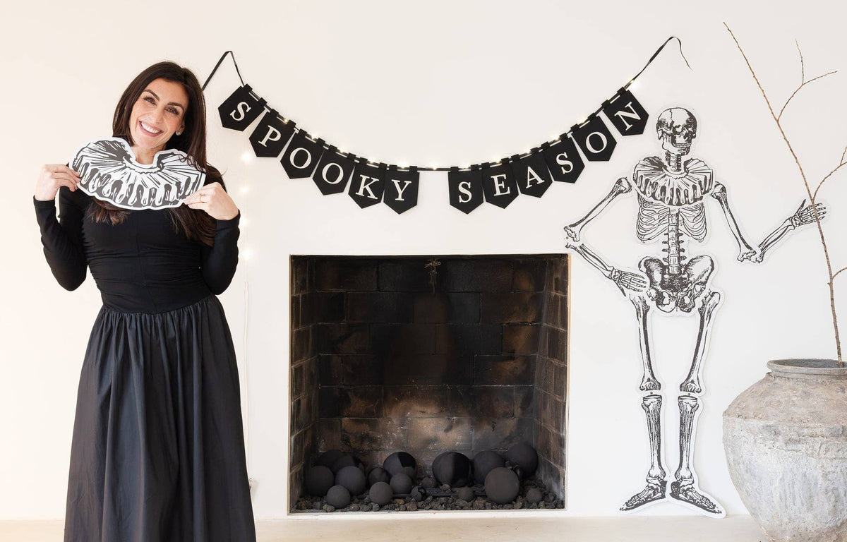 Woman beside a 'Spooky Season' banner with a skeleton decoration hung in beside of a fireplace.