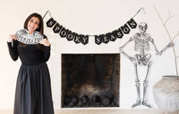 Woman beside a 'Spooky Season' banner with a skeleton decoration hung in beside of a fireplace.